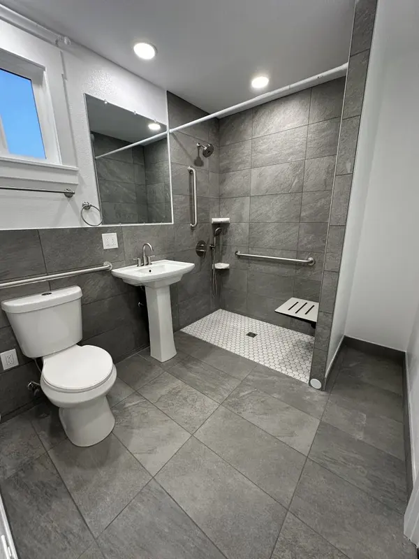 Accessible bathroom with grab bars, a pedestal sink and a curbless roll-in shower