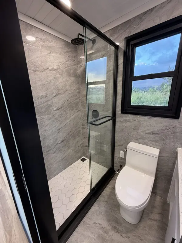 Glass walk-in shower with hexagon floor tile and a window onto open land