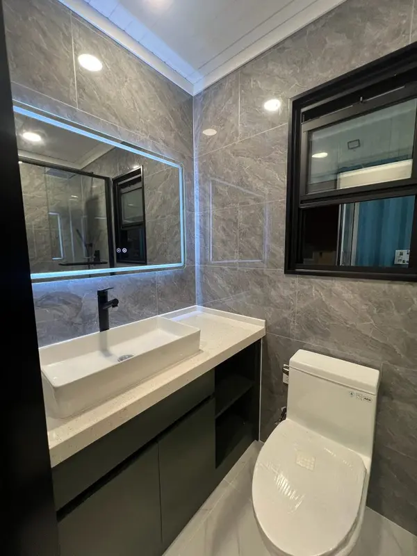 Grey-tiled bathroom with a long white vessel sink and a backlit mirror