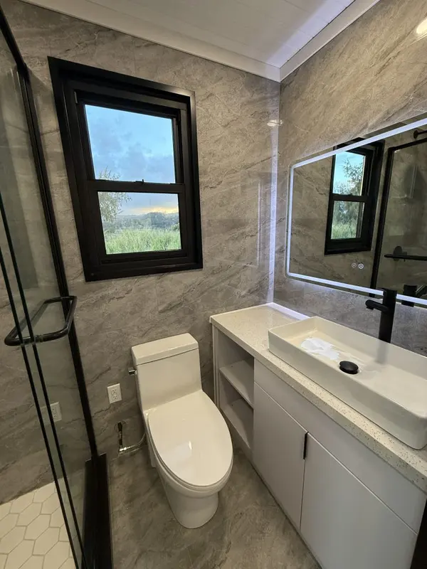 Bathroom with a white vanity, a backlit mirror and grey stone-look walls