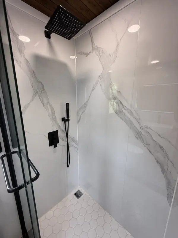 Walk-in shower with marble-look panels, black fixtures and hexagon floor tile