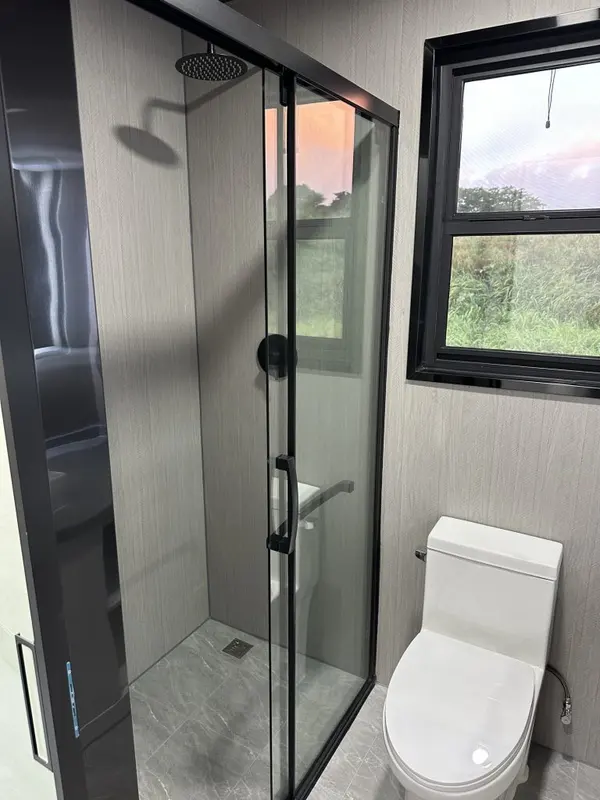 Glass shower with a rain head next to a black-framed window