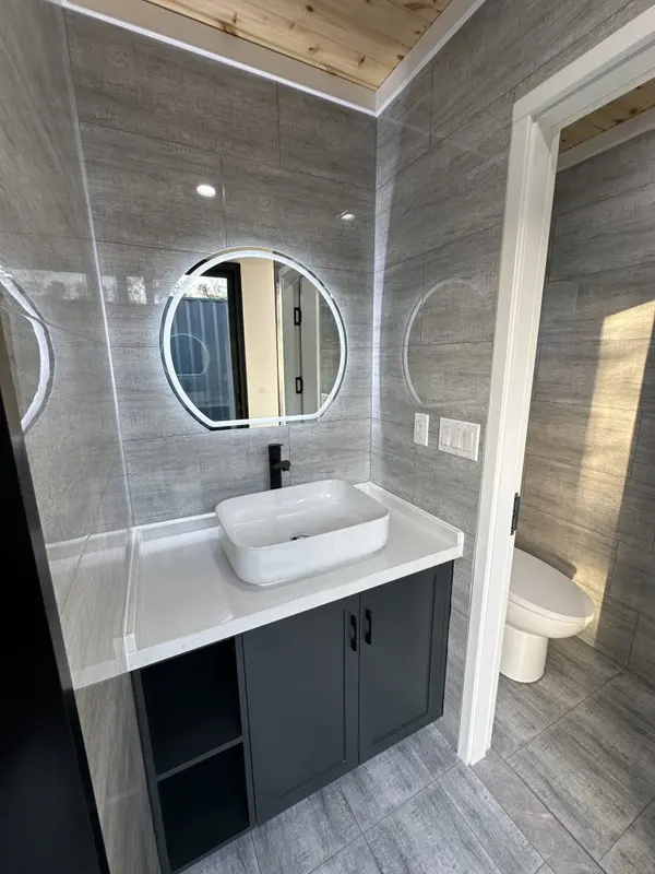 Vanity with a round backlit mirror, a vessel sink and a charcoal cabinet