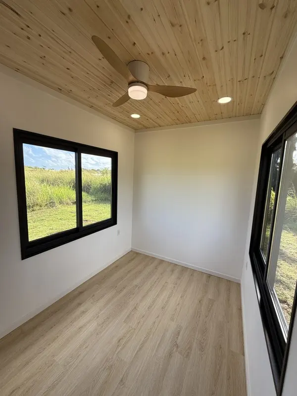 Bedroom with a pine ceiling and black-framed windows onto green pasture