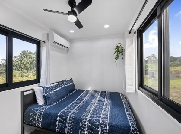 Bedroom with navy bedding, a wall air conditioner and windows on two sides