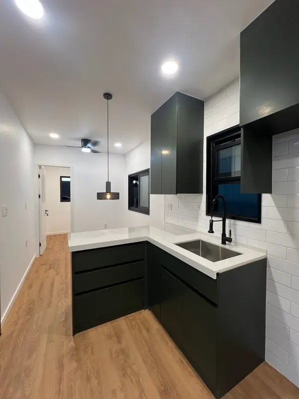 Dark green kitchen with white subway tile, a black faucet and a warm wood floor
