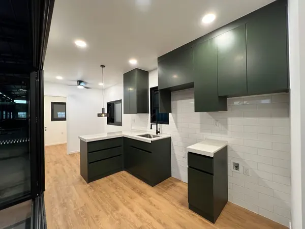 Dark green and white L-shaped kitchen with tall cabinets and a wood floor