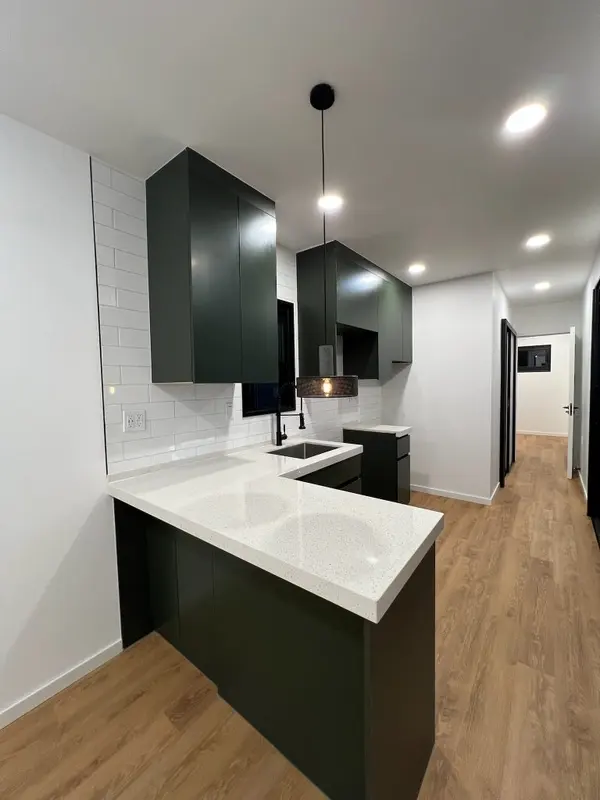 Dark green kitchen with a white quartz peninsula and a hallway beyond