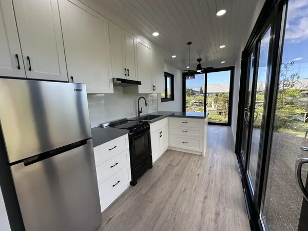 Long white kitchen with a stainless fridge beside a wall of glass doors