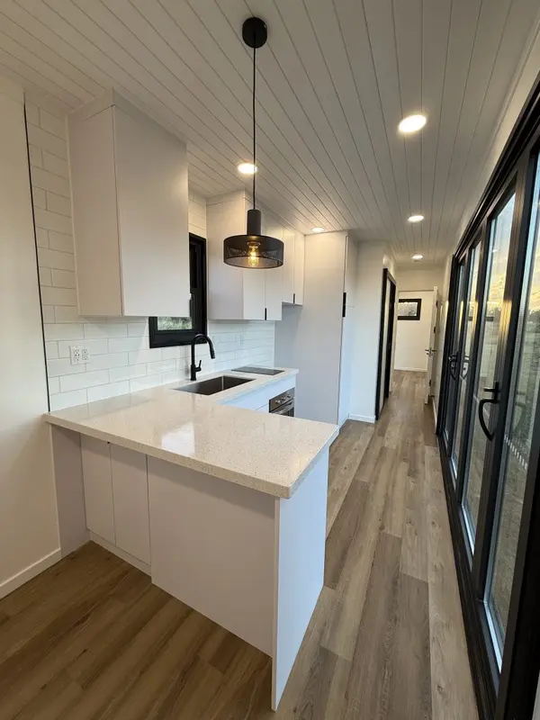 White kitchen peninsula under a black pendant light, beside full-height glass doors