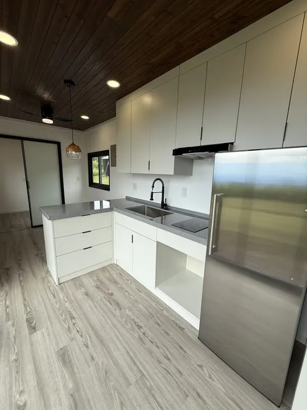 White kitchen with a stainless fridge and grey counters under a dark wood ceiling