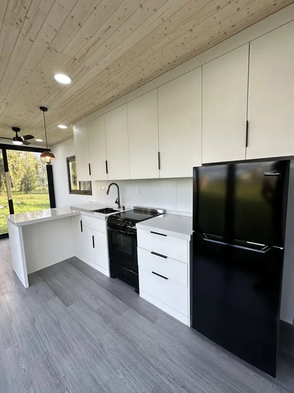 White L-shaped kitchen with a black fridge and range, open to a glass door