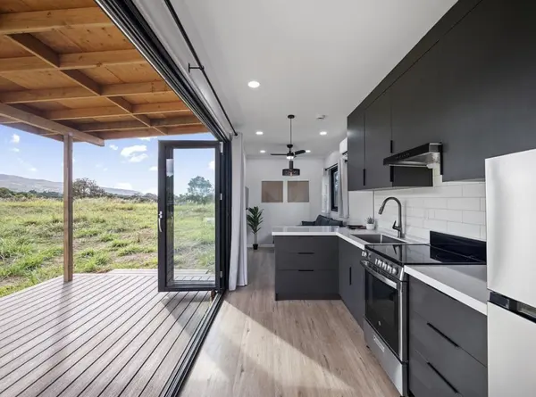 Kitchen and living space opening through folding glass doors onto a covered deck and field