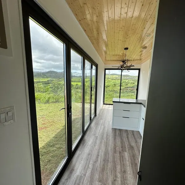 Room with a wall of black-framed glass doors looking out over green hills