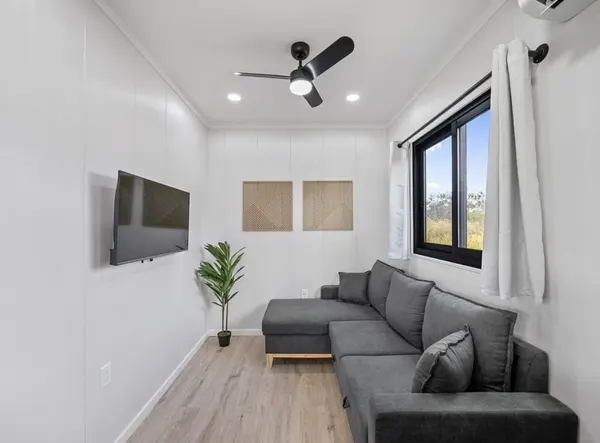 Living room with a grey sectional, a wall-mounted TV and a black-framed window