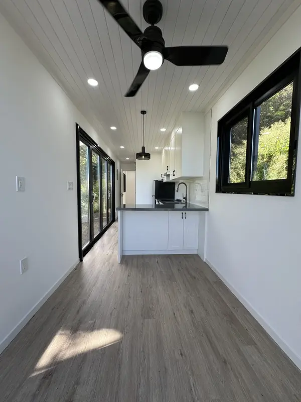 Open room with black-framed windows and glass doors, and a white kitchen at the far end