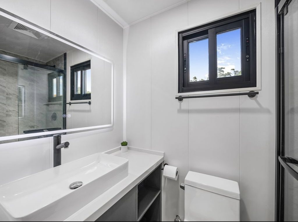 Bright bathroom with a long white vessel sink, wide mirror and a window