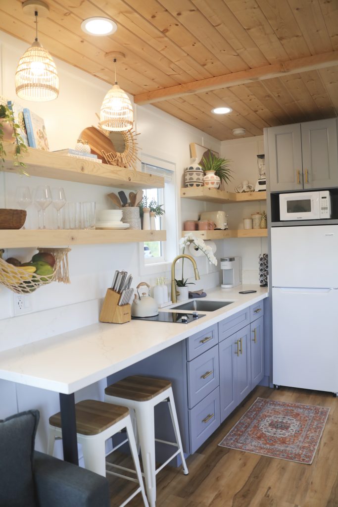 Kitchen with blue-grey cabinets, open wood shelves and white bar stools