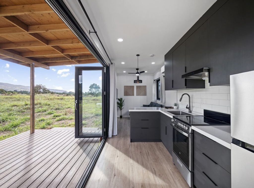 Dark kitchen opening through folding glass doors onto a covered deck and open field