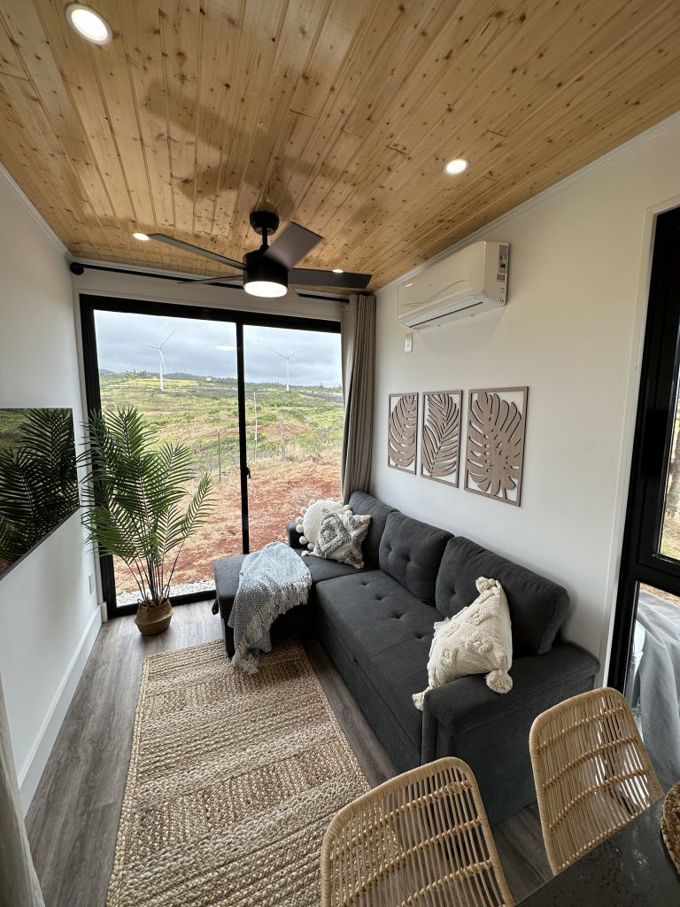Living area with a grey sofa, rattan chairs and a sliding glass door looking out to green hills